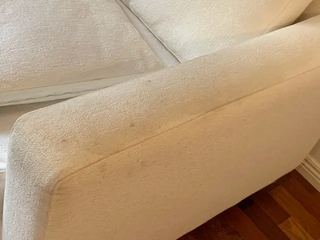 Vaalean bouclé-sohvan likaantunut käsinoja ennen pesua.